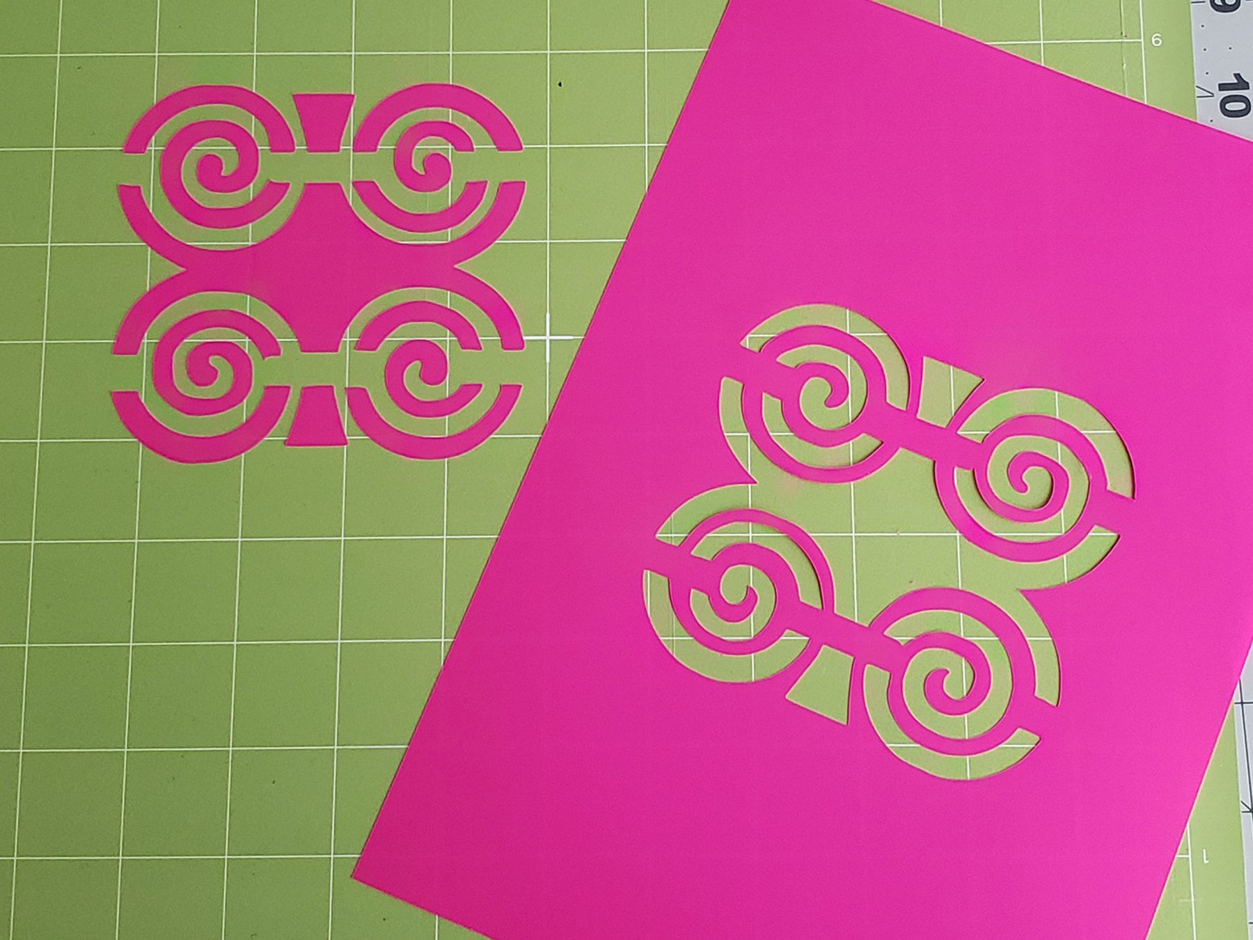 Pink plastic stencil sheets with cut-out Dwennimmen symbols on a green cutting mat