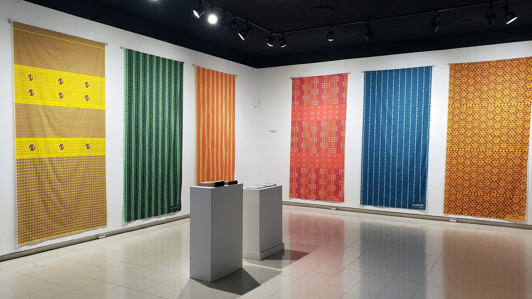 The Lessons from Granny exhibition at Ohio University: long printed cloths in yellow, green, orange, red and blue hang along white gallery walls