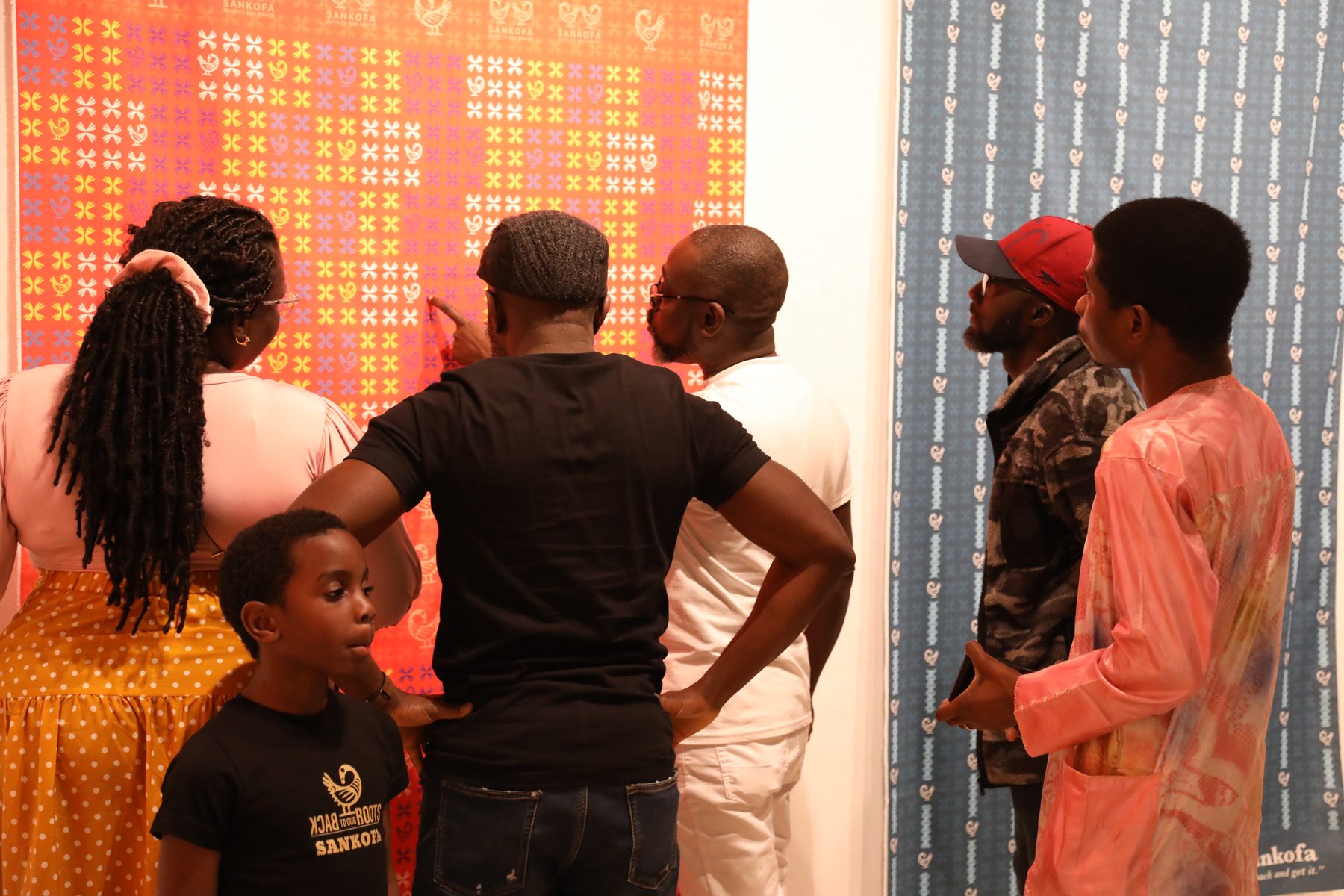Visitors, including a child, looking closely at a red printed cloth during the Lessons from Granny exhibition